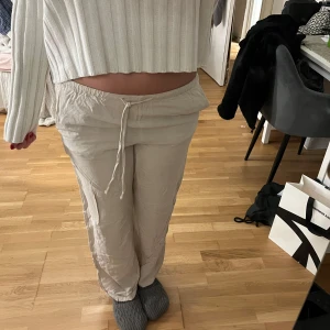 Beiga mjukisbyxor med dragsko - Säljer ett par beiga linnebyxor med dragsko i midjan. Byxorna har en avslappnad passform och är perfekta för en chill stil. Tillverkade i mjukt material och har utsvängda ben. Superbekväma och lätta att matcha med olika toppar.