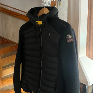 Svart pufferjacka från Parajumpers - Helt ny jacka, väldigt snygg och stilren!Säljer en svart pufferjacka från Parajumpers med huva och dragkedja. Jackan har en gul detalj vid halsen och klassisk Parajumpers-logga på ärmen. Perfekt för kyliga dagar och har en sportig look.
