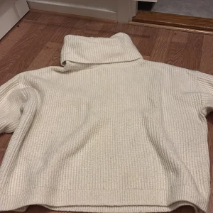 Vit stickad polotröja - Säljer en mysig vit stickad polotröja med hög krage. Tröjan har lång ärm och är ribbstickad vilket ger en snygg struktur. Perfekt för kyliga dagar och enkel att matcha med olika outfits.