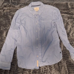 Blåvit randig skjorta från Holly & Whyte - Klassisk blåvit randig skjorta från Holly & Whyte by Lindex. Skjortan har långa ärmar, knappar framtill och en bröstficka. Perfekt för en stilren look och tillverkad i mjuk bomull.