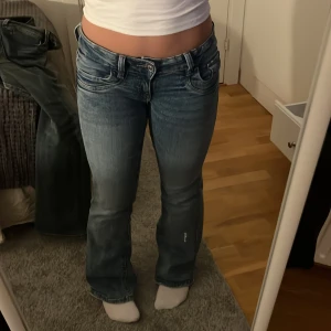 Lågmidjade bootcut jeans i ljusblå denim - Säljer ett par lågmidjade bootcut jeans i ljusblå denim med klassiska fem fickor och knappgylf. Jeansen har en lätt tvättad look och sitter snyggt över höfterna. Perfekta för dig som gillar retrostil!