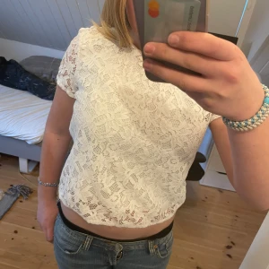Vit spetsblus från Hugo Boss - Säljer en söt vit spetsblus från Hugo Boss. Blusen är croppad med korta ärmar och har ett fint spetsmönster över hela. Dragkedja bak för enkel påklädning. Perfekt att styla med jeans eller kjol!knappt använda org pris:2000kr