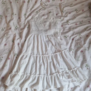 Vit sommarkllänning med spetsdetaljer - Säljer en så fin vit sommarklänning med virkade spetsdetaljer upptill och volanger i kjolen. Klänningen har halterneck och knytning i ryggen med en öppen rygg. Perfekt för sommaren och semester!❤️