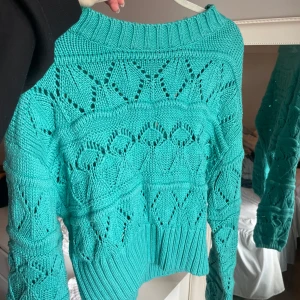 Turkos stickad tröja med hålmönster - Säljer en turkos stickad tröja med snyggt hålmönster och bred ribbad kant vid hals, ärmslut och nederkant. Tröjan har lång ärm och en lite lösare passform. Perfekt för lager-på-lager-stil!