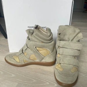 Beige sneakers med kardborre från Isabel Marant - Säljer nu ett par beiga skor ifrån Isabel Marant. Skorna är av både mocka och skin. Sparsamt använda!! Skorna har en liten fläk på insidan av hälen, men den syns knappt! Skorna är storlek 37 men skulle säga att dem passar nån med st 36 mer. Medhavd låda till skorna!!💖
