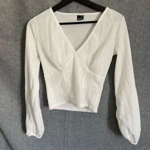 Vit topp med v-ringning - Säljer en vit topp med v-ringning och långa ärmar. Toppen har en lätt strukturerad yta och sitter snyggt i midjan. Perfekt att styla med jeans eller kjol.