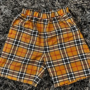 Gula rutiga shorts med resårmidja - Snygga shorts i gult med svart, vitt och rött rutmönster. De har en bekväm resår i midjan och är perfekta för varma dagar. Passar dig som gillar en avslappnad och trendig stil.