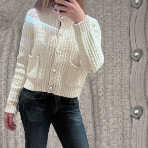 Vit stickad kofta från Kappahl - Söt crème/beige stickad kofta från Kappahl med pärlknappar och två fickor framtill. Väldigt detaljerad och fin stickning som ni kan se.  Använd mycket få gånger. 