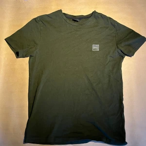 Mörkgrön t-shirt från BOSS - Säljer en stilren mörkgrön t-shirt från BOSS med rund halsringning och diskret logotyp-patch på bröstet. Perfekt för en enkel och snygg look.