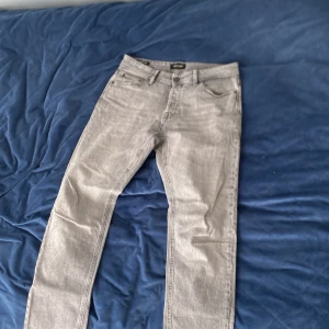 Grå jeansbyxor - Säljer ett par grå jeansbyxor med klassisk femficksdesign och raka ben. Byxorna har normal passform och stängs med dragkedja och knapp. Perfekta till vardags och enkla att matcha med olika stilar.