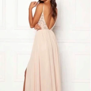 Ljusbeige/rosa långklänning med pärldetaljer - Långklänning med smala axelband, djup rygg och v-ringning. Överdelen är dekorerad med pärlor och paljetter, kjolen är luftig med slits framtill. Perfekt för bal eller fest. Storlek 36. Aldrig använd. Lapp kvar. 