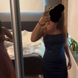 Mörkblå långklänning från Nelly - Säljer en elegant mörkblå långklänning från Nelly med smala axelband och öppen rygg. Klänningen har en tight passform och är tillverkad i ett glansigt satin material. Perfekt för speciella tillfällen! Har endast använt den i två timmar och inte förstörd!