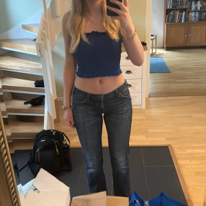 Blå tubtopp med volangdetaljer - Säljer en blå tubtopp med volangdetaljer upptill och nedtill. Toppen har en smockad design som ger en stretchig och bekväm passform. Perfekt för sommarens varma dagar!