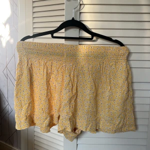 Gula blommiga shorts från Mango - Söta gula shorts från Mango med vitt blommönster och bred resår i midjan. Lätta och luftiga med fickor, perfekta för varma dagar. Passar dig som gillar en avslappnad och somrig stil.
