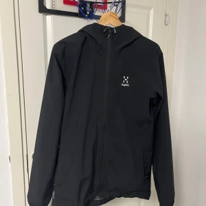 Haglöfs jacka - Säljer en svart Haglöfs skaljacka i storlek S. Enkel och stilren design med justerbar huva och dragkedja framtill. Jackan är lätt och smidig – perfekt som ytterlager under vandring, löpning eller till vardags. Vattentålig och vindtät med bra andnings