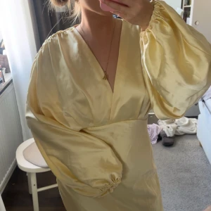 Ljusgul långklänning med ballongärmar - Säljer en elegant ljusgul långklänning i satin med v-ringning och voluminösa ballongärmar. Klänningen har en figurnära passform i midjan och ett mjukt, glansigt material som ger en lyxig känsla. Perfekt för speciella tillfällen. Köpt begagnat men aldrig använd av mig, det finns lite slitningar, bilder syns i slutet. Storlek 40 men passar mig som är 38