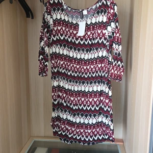 Mönstrad klänning från Divided - Säljer en helt ny klänning från Divided med grafiskt mönster i vinrött, svart och vitt. Klänningen har trekvartsärm och rund halsringning. Cut-outs på armar.