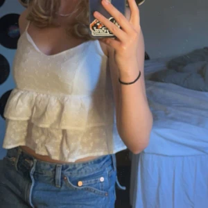 Vit croppad linnetopp med volang - Säljer en söt vit croppad linnetopp med tunna axelband och volangdetalj. Toppen har broderat hålmönster och är perfekt för varma dagar. Lappen är borta så vet ej exakt storlek, har för mig att det är M (sitter bra på mig som är M)🥰