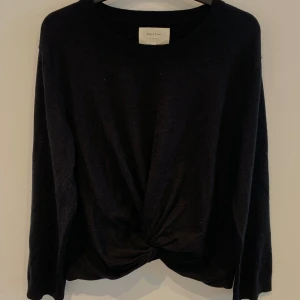 Svart långärmad tröja med twist från Part Two - Säljer en svart långärmad tröja från Part Two i mjukt material. Tröjan har en snygg twist-detalj framtill och rund halsringning. Perfekt för en stilren och enkel look.
