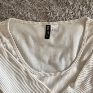 Vit ribbad långärmad topp från HM - Säljer en vit ribbad långärmad topp från HM. Toppen har en djup rundad ringning och är croppad i modellen. Perfekt att styla med jeans eller kjol för en enkel och snygg look.