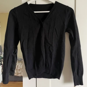 Svart kofta med knappar - En klassisk svart kofta med v-ringning och knäppning framtill. Långärmad modell med ribbade muddar vid ärmslut och nederkant. Perfekt att slänga över en topp eller klänning, sjukt söt🩷