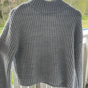 Grå ribbstickad tröja från Kappahl - Säljer en grå ribbstickad tröja från Kappahl med hög krage. Tröjan är croppad och har långa ärmar, perfekt för kyligare dagar. Enkel och stilren design som passar till det mesta.