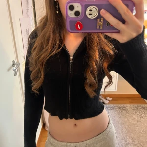 Svart croppad hoodie med dragkedja💕 - Intressekoll på en svart croppad hoodie med dragkedja framtill. Tröjan har långa ärmar och är ribbad i materialet. Perfekt för en avslappnad och trendig look.🥰Skriv vid frågor eller för fler bilder!