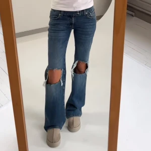 Blå bootcut jeans med hål vid knäna - Snygga blå bootcut jeans med stora slitningar vid båda knäna. Jeansen är endast använda en gång då dom är för små för mig