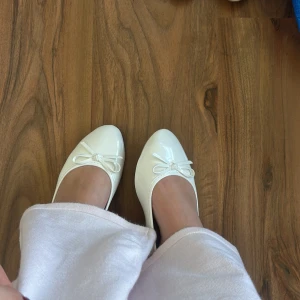 Vita ballerinaskor med rosett - Säljer ett par stilrena vita ballerinaskor med rund tå och söt rosettdetalj framtill. Skorna har en platt sula och är perfekta för dig som gillar en klassisk och enkel look. Säljer ena paret då jag råkat beställa 2 par 