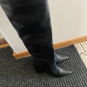 Svarta höga stövlar med klack - Säljer ett par svarta, höga stövlar i skinnimitation med spetsig tå och klack. Stövlarna går över knäet och har en elegant, stilren design som passar till många outfits. Priset går att diskutera🫶🏻