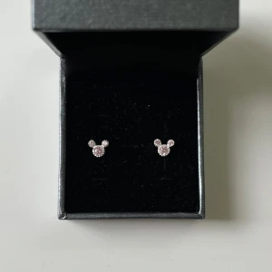 Silver örhängen  - Små äkta silver  örhängen i form av Musse Pigg-huvuden, dekorerade med ljusrosa glittrande stenar. I helt nytt skick.