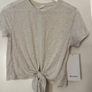  knyt-topp från Lululemon - Superskön och luftig ljusbeige topp från Lululemon med korta ärmar och knytning framtill. Tunt, lätt material med lite transparent känsla och relaxed fit. 