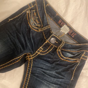 Vintage jeans - Säljer ett par mörkblå jeans från Hydraulic med riktigt feta kontrastsömmar i gult och orange. Jeansen har snygga fickdetaljer med knappar och broderier både fram och bak. Klassisk femficksmodell och cool faded effekt på låren. Dom är skinny men går lätt att sy ut!