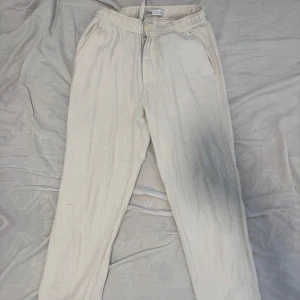Beiga linnebyxor från Zara - Beiga linnebyxor från Zara med elastisk midja och raka ben. Byxorna har sidfickor fram och två bakfickor. Sköna och avslappnade, perfekta för chill dagar. Tillverkade i mjukt bomullsmaterial.