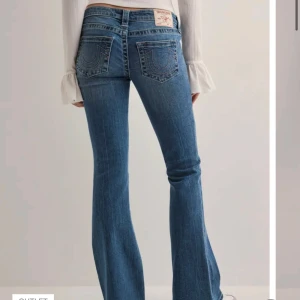 True Religion jeans - Snygga blå jeans från True Religion x nelly med klassiska kontrastsömmar och ikoniska bakfickor. Modellen har bootcut-ben, låg midja och normal passform. Dom är i storlek 26🫶 Endast använd ett fåtal gånger därmed är dom nyskick