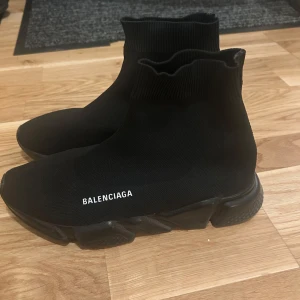 Svarta Balenciaga Speed Trainer sneakers - Svarta Balenciaga Speed Trainer sneakers med strumpliknande ovandel i stretchig textil och chunky svart sula. Minimalistisk design med vit Balenciaga-logga på sidan. Skorna har rund tå och platt sula för en clean och modern look.