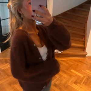 Brun fluffig kofta med knappar - Nypris 992 kr💓 Mysig brun kofta med fluffig känsla och stora pärlemorknappar. Koftan har en loose passform och långa ärmar, perfekt att slänga över en topp. Materialet känns stickat och ger en chill vibe till outfiten.