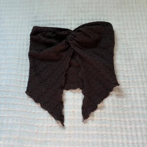 Brun bandeau tubtopp från SHEIN - Säljer en brun bandeau tubtopp från SHEIN i storlek XS. Toppen har en snygg struktur med broderad känsla, knutdetalj framtill och spetsiga kanter nertill. Gjord i stretchig polyester som sitter tajt och bekvämt. Perfekt för dig som vill sticka ut med en unik topp!