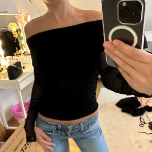 Svart mesh offshoulder topp - Säljer en svart offshoulder topp i mesh med långa ärmar. Toppen har tight passform och snygga rynkade detaljer både fram och bak. Perfekt för dig som gillar en stilren men ändå trendig look. 