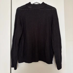 Svart stickad tröja från Vero Moda - Mysig svart stickad tröja från Vero Moda med grovstickat mönster och hög ribbad krage. Tröjan har långärmad passform och är perfekt för kyliga dagar. Enkel att styla med jeans eller kjol för en chill look.