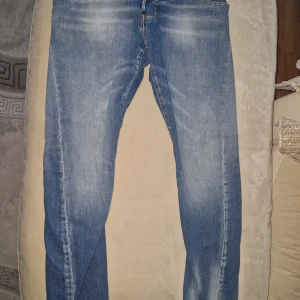 Blå Dsquared2 jeans med slitningar - Storlek 16y,176c. Blå jeans från Dsquared2 med ljusa slitningar och klassisk femficksdesign. Jeansen har normal passform, raka ben och tydliga detaljer som läderpatch bak och Dsquared2-logga vid fickan. Perfekta för dig som gillar en avslappnad men trendig look.