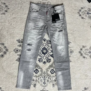 Dsquared2 jeans - Snygga grå jeans från Dsquared2 med slitningar och färgstänk för en edgy look. Jeansen har klassisk femficksdesign, låg midja och Dsquared2-logga på både etikett och bakficka. Perfekta för dig som gillar streetstyle och detaljer.