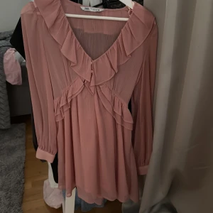 Rosa volangklänning från Zara - Supersöt kort rosa klänning från Zara med v-ringning och volangdetaljer både fram och bak. Långärmad modell i ett lätt  tyg som ger en luftig känsla. 