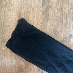 Svarta raka jeans med hög midja - Snygga svarta jeans med hög midja och raka ben. Klassisk femficksmodell med dragkedja och knapp framtill. Jeansen är i ett mjukt denimtyg som sitter skönt och passar till allt. Perfekta för dig som gillar en clean och stilren look.