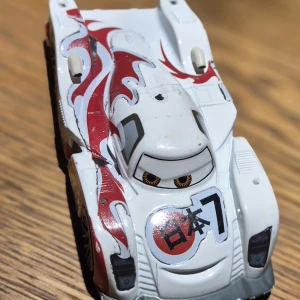 Fin metllbil ifrån filmen cars/bilar - Bilderna visar en leksaksbil inspirerad av filmen Cars, med japanska tecken och racingdesign. Det är ingen bok på bilderna, utan en samlarbil med detaljerade dekaler och sportig look. Perfekt för fans av bilar och animerade filmer. Bilen är inköpt på Disney store I USA. 