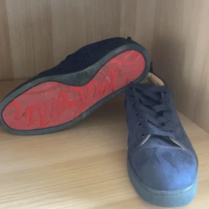 Mörkblå Louboutin skor - Snygga mörkblå sneakers i mocka från Christian Louboutin med klassisk röd sula och mörkblå snören. Mycket bra skick och har bara använt dem några gånger. Perfekt för dig som vill sticka ut med en exklusiv touch. Ikonisk design och lyxig känsla. Tvätt på skorna sker såklart innan jag skickar dom! Pris ej hugget i sten!