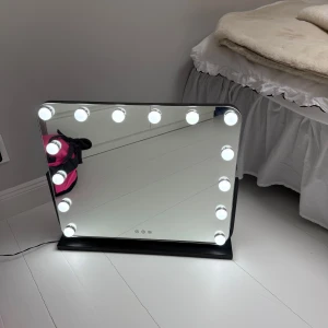 Stor sminkspegel med LED-belysning - Säljer en stor, rektangulär sminkspegel med svart ram och ställning. Spegeln har 14 LED-lampor runt kanten som kan justeras mellan kallt och varmt ljus via touchknappar. Perfekt för att få till flawless makeup och detaljerad styling.