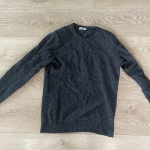 Mörkgrå stickad tröja J.Lindeberg - Mysig mörkgrå stickad tröja från J.Lindeberg i klassisk modell med rund halsringning och ribbade muddar. Perfekt för lager-på-lager och passar till allt. Skön och stilren, enkel att matcha med jeans eller chinos.