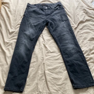 Nudie Jeans Grim tim - Säljer ett par svarta jeans från Nudie Jeans i klassisk rak modell. Jeansen har fem fickor, snygga sömmar och är tillverkade i mjukt bomullstyg. Perfekta för dig som gillar en stilren och enkel look.
