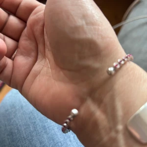 Caroline Svedbom armband  - Ett tunt och stilrent armband i silverfärg med små rosa stenar längs hela bandet. Armbandet är öppet och justerbart, perfekt för att ge en färgklick till din look. Snyggt att bära ensamt eller tillsammans med andra armband för en personlig stil. Ingår låda , hämta i Majorna Gbg 